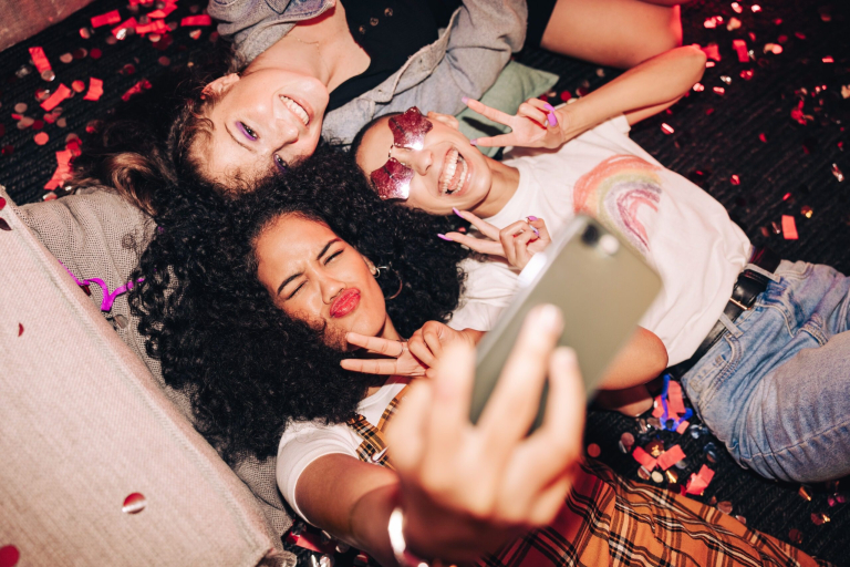 Capturing crazy party moments. Top view of three happy friends taking a selfie while lying on the floor at a house party. Group of cheerful female friends having fun together on the weekend.