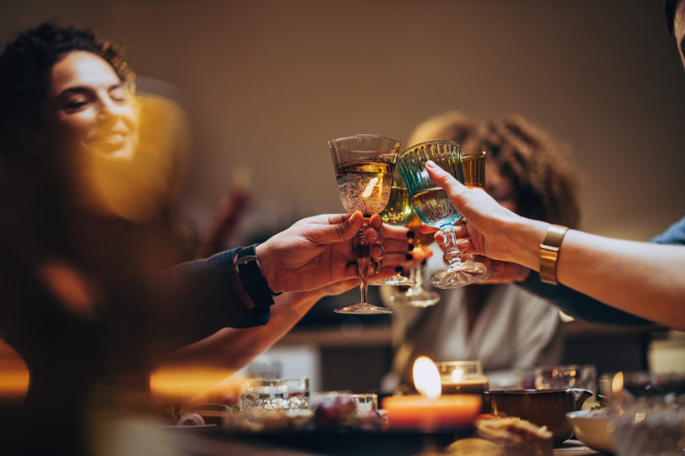 Unrecognizable group of multi-ethnic people having fun at dinner party and toasting with alcohol.