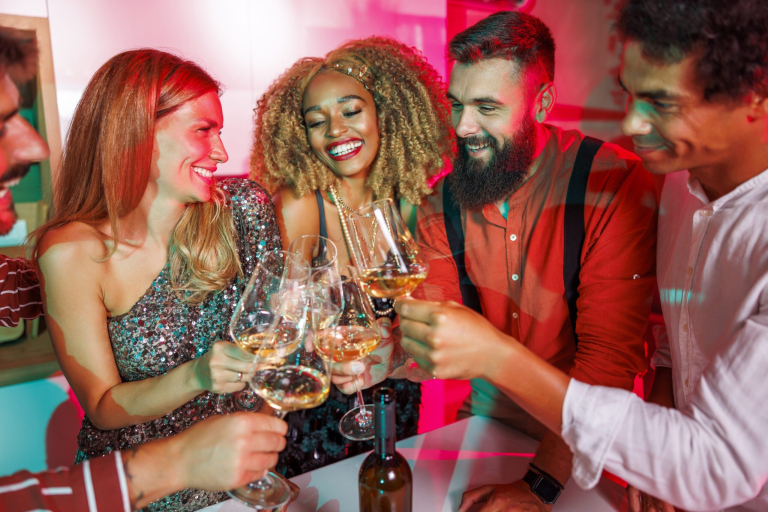 Group of cheerful young friends having fun at house party, making a toast raising glasses of wine, dancing and drinking